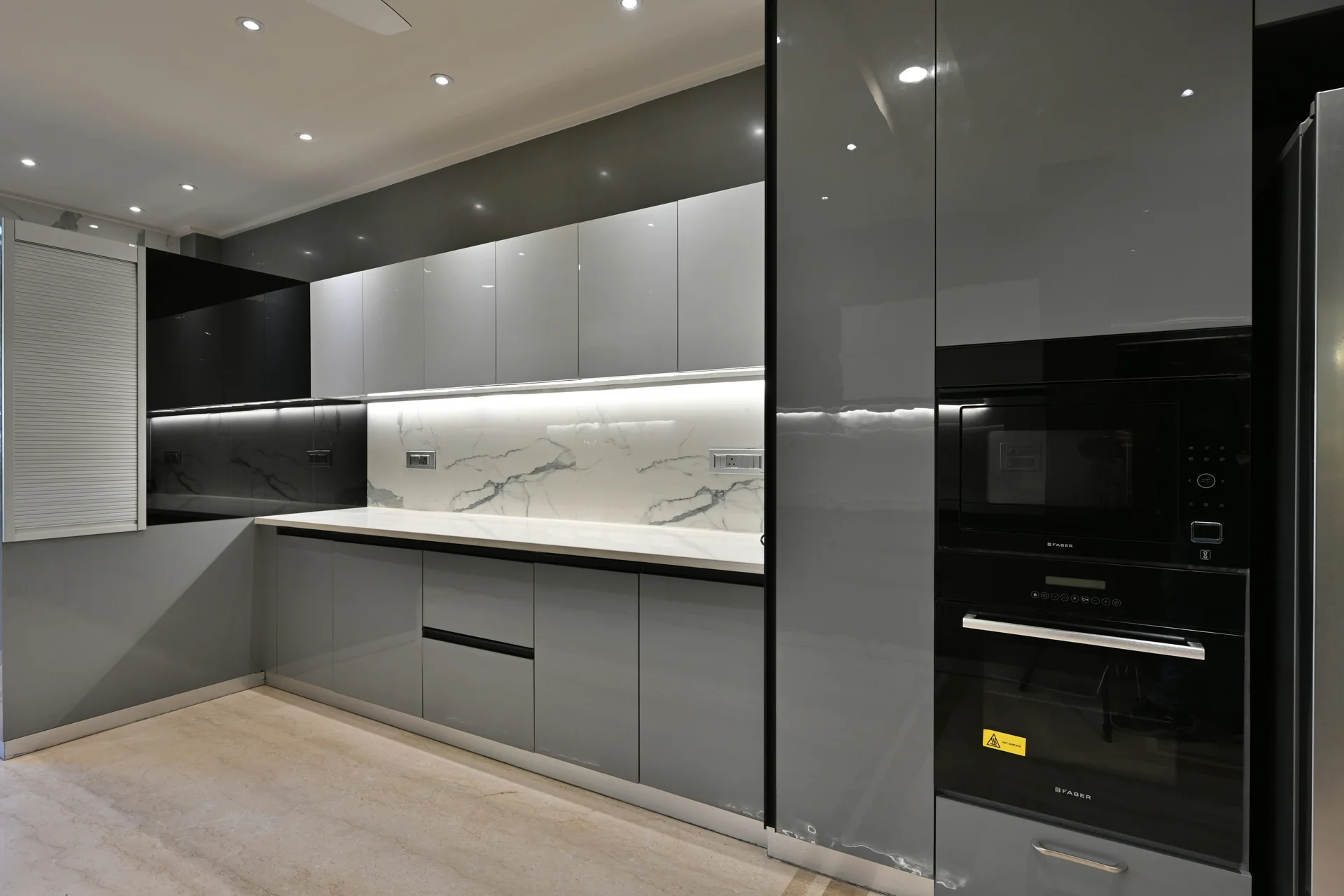 Modern modular kitchen with handleless high-gloss grey cabinets and a marble backsplash